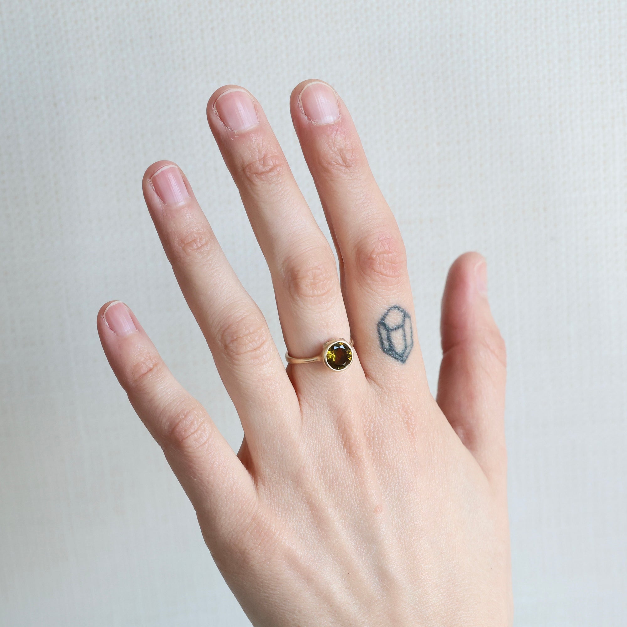 Hand wearing a ring with a green gemstone on a neutral background