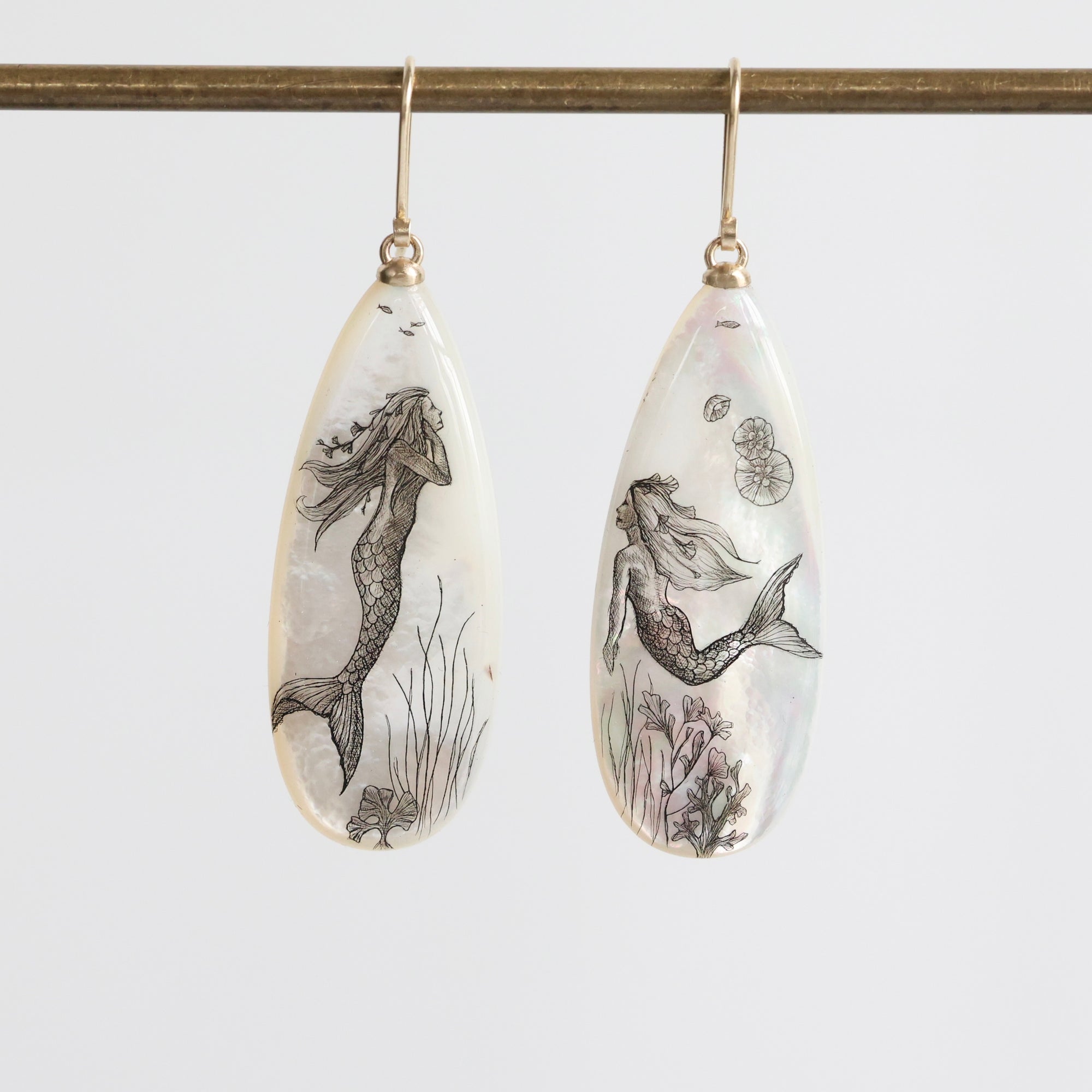 Teardrop-shaped earrings with mermaid designs on a white background