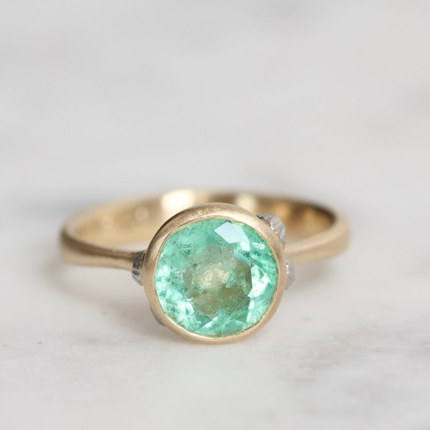 Gold ring with a green gemstone on a light gray background