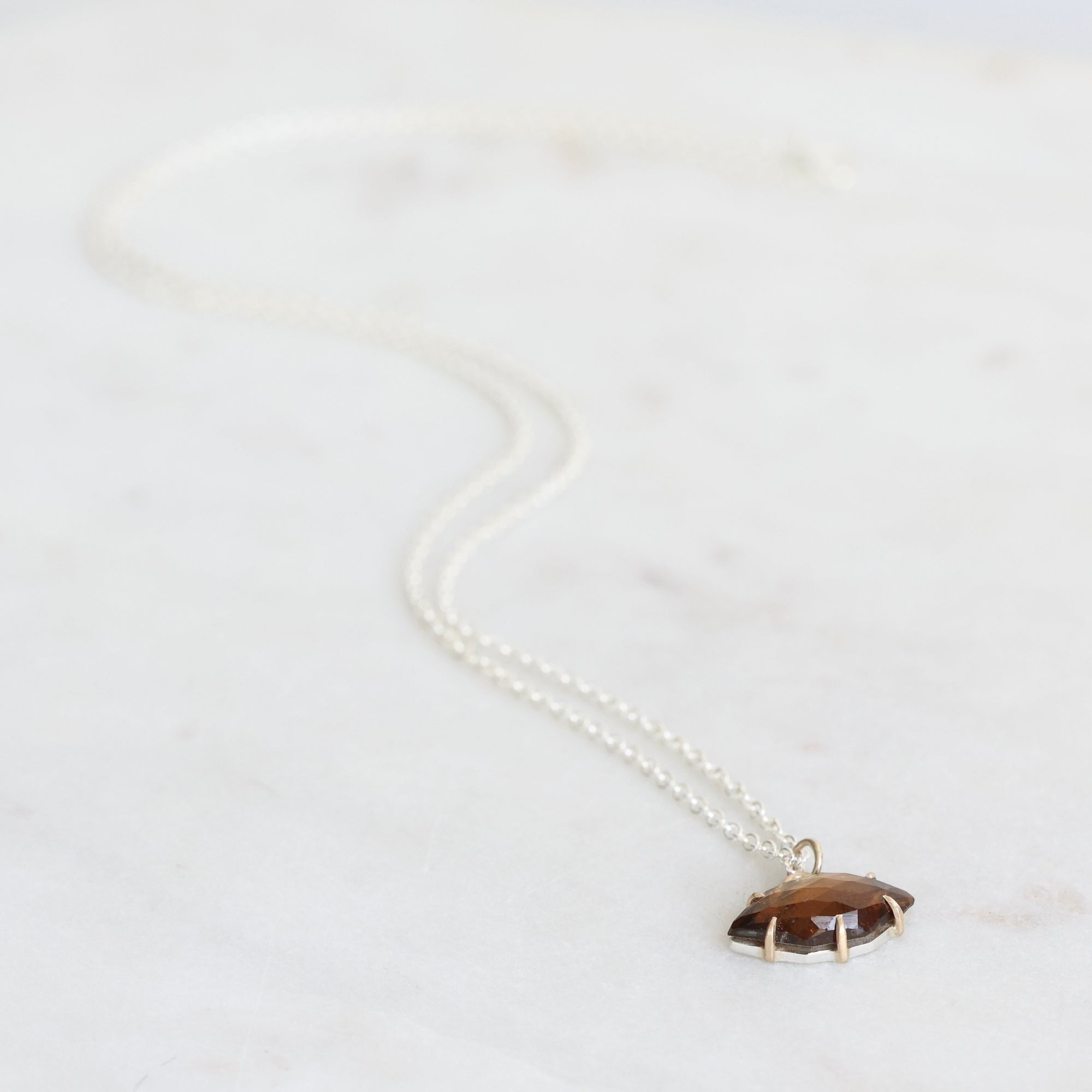 brown pendant on silver chain laying on gray background