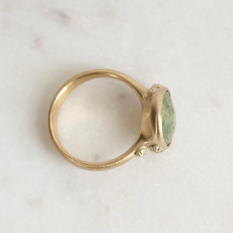 Gold ring with a green gemstone on a light gray background