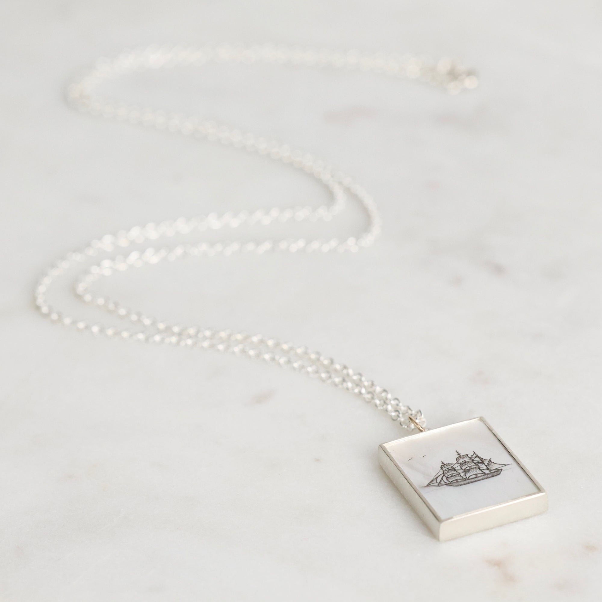Necklace with a square pendant featuring a ship design on a light background