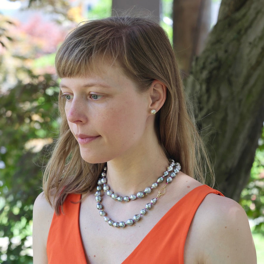 Woman wearing a pearl necklace outdoors with greenery in the background