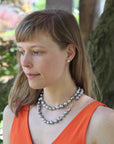 Woman wearing a pearl necklace outdoors with greenery in the background