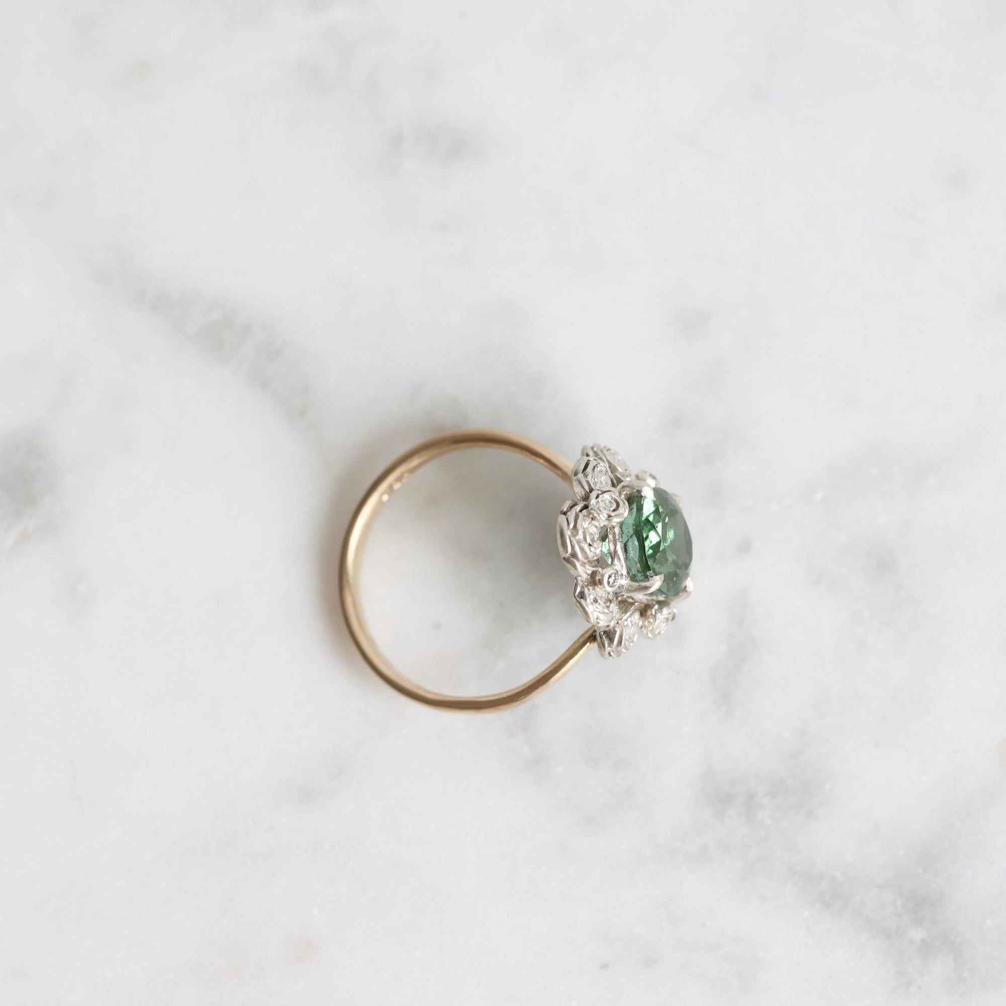 Gold ring with a green gemstone on a marble surface