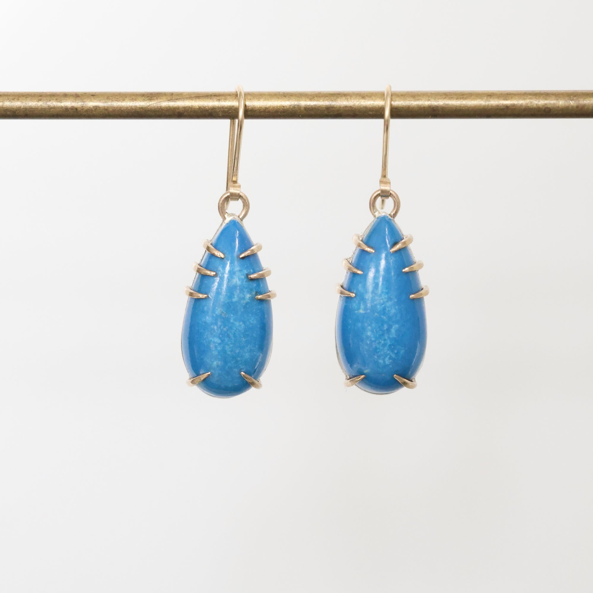 Pair of blue teardrop earrings with gold accents on a white background