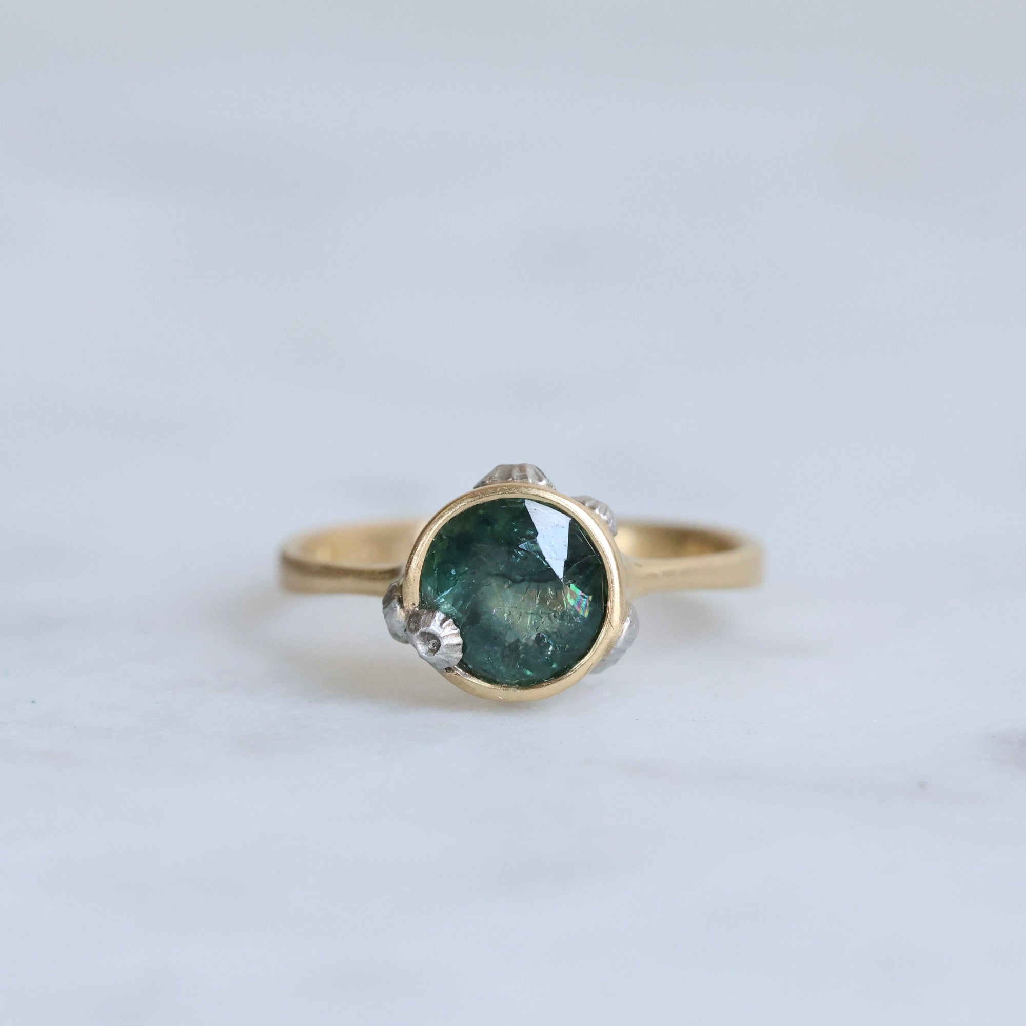 Gold ring with a green gemstone on a light gray background