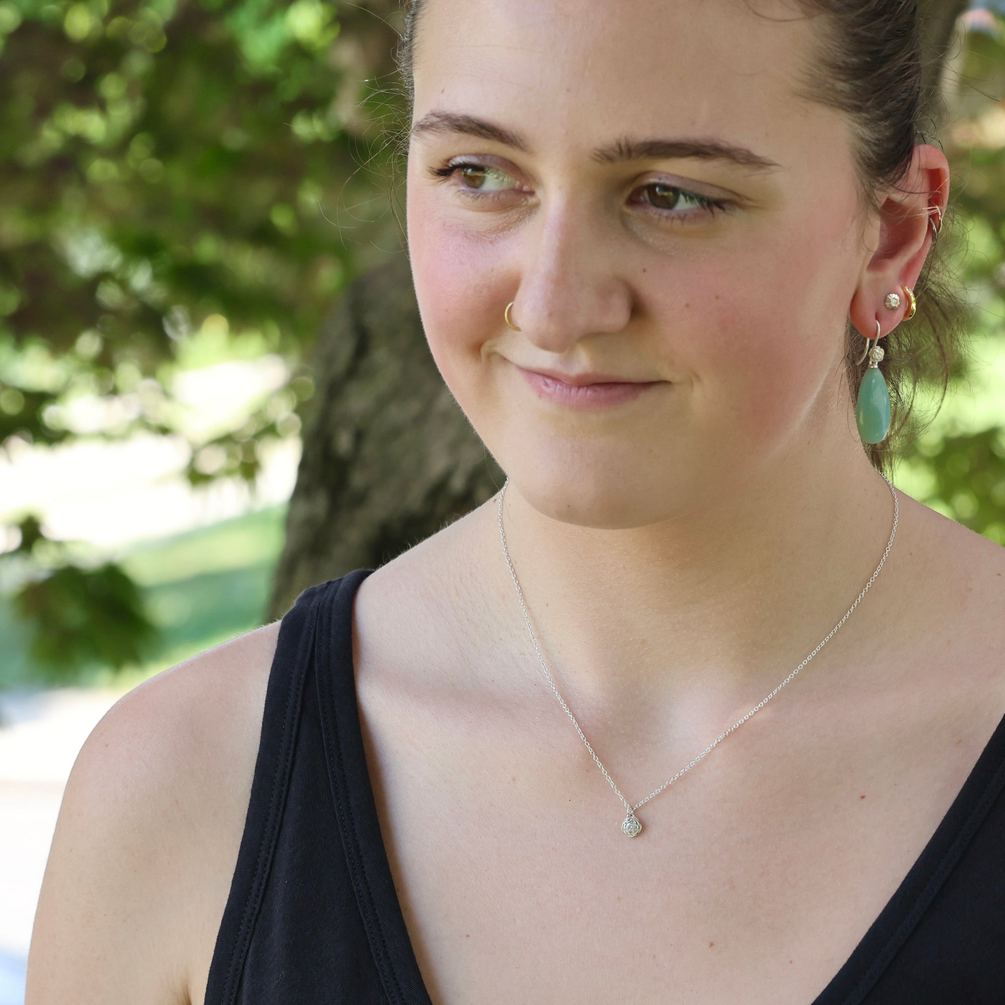Woman wearing a black top and green earrings with a blurred natural background