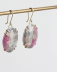 Pair of earrings with pink and gray gemstones on a gold hook against a white background