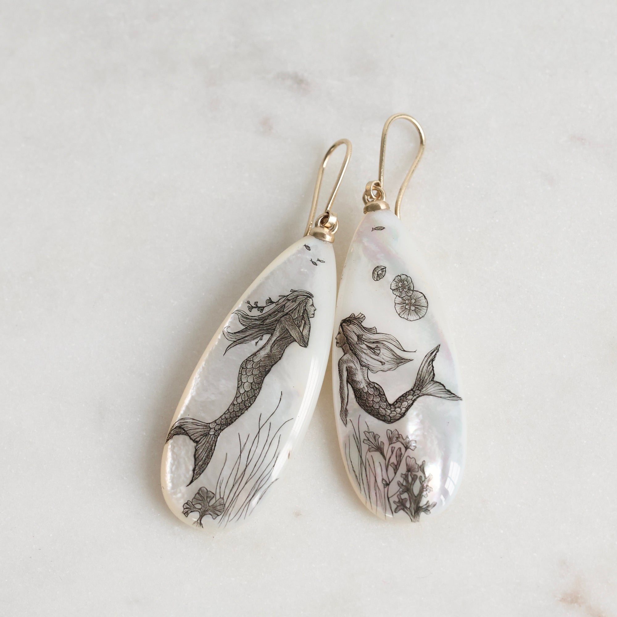 Teardrop-shaped earrings with mermaid designs on a light background