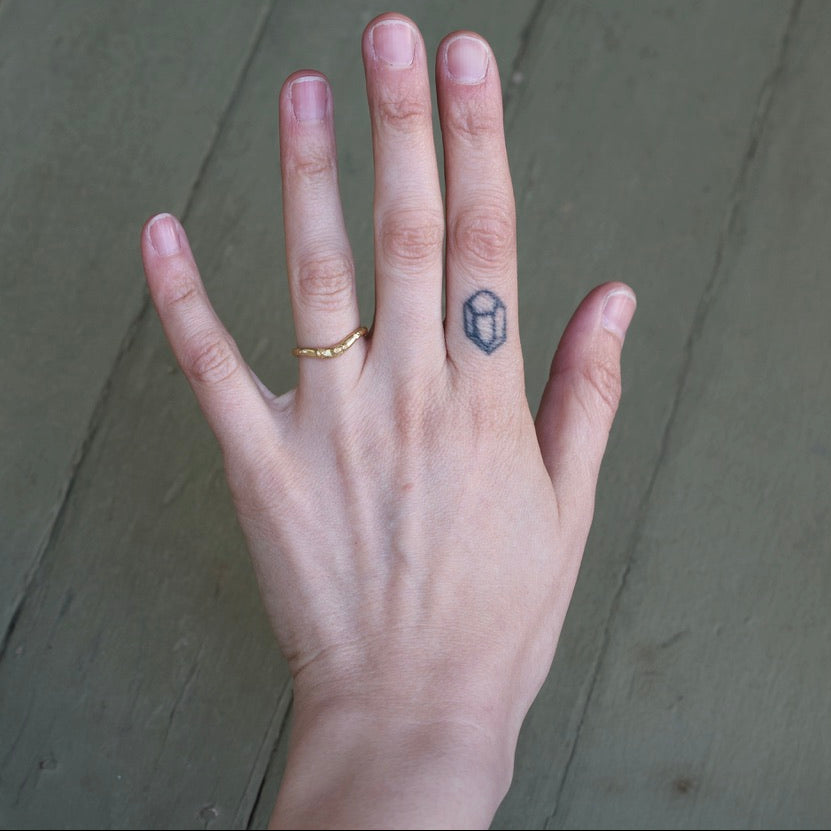 Hand with a gold ring and hexagonal tattoo on a neutral background
