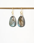A pair of teardrop-shaped labradorite drop earrings with gold hooks, hanging from a gold rod against a clean white background.