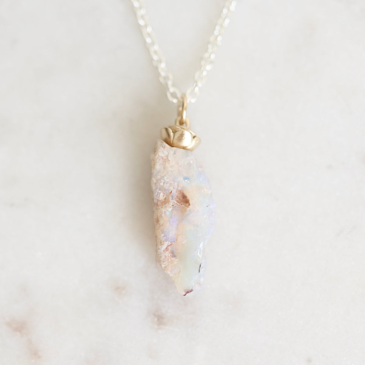 Light colored fossilized opal with gold rose detail suspended from a silver chain against a white background.