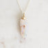 Light colored fossilized opal with gold rose detail suspended from a silver chain against a white background.