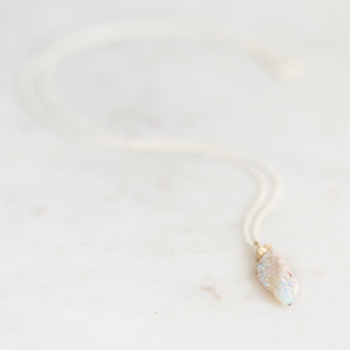 Light colored fossilized opal with silver chain and gold cap on a marble background.
