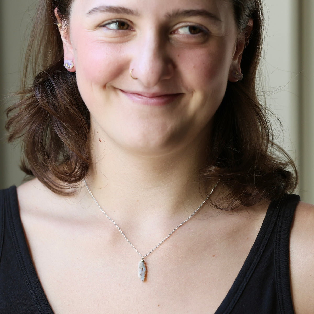Woman smiling wearing raw opal necklace against an indoor background.