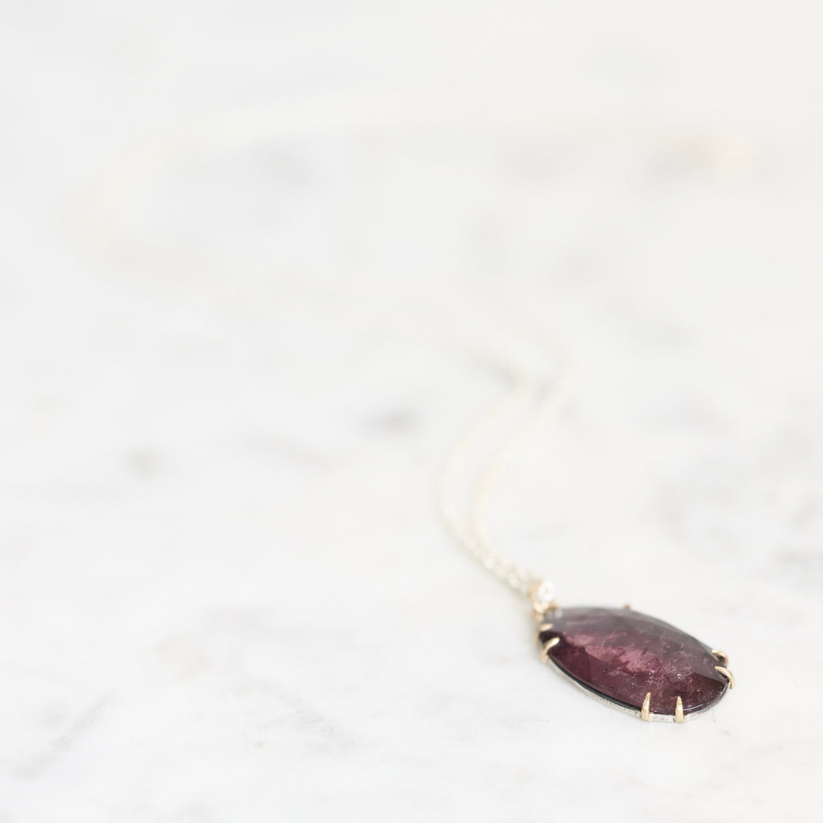Purple pendant necklace laying against pale background