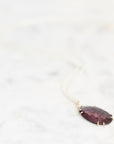 Purple pendant necklace laying against pale background