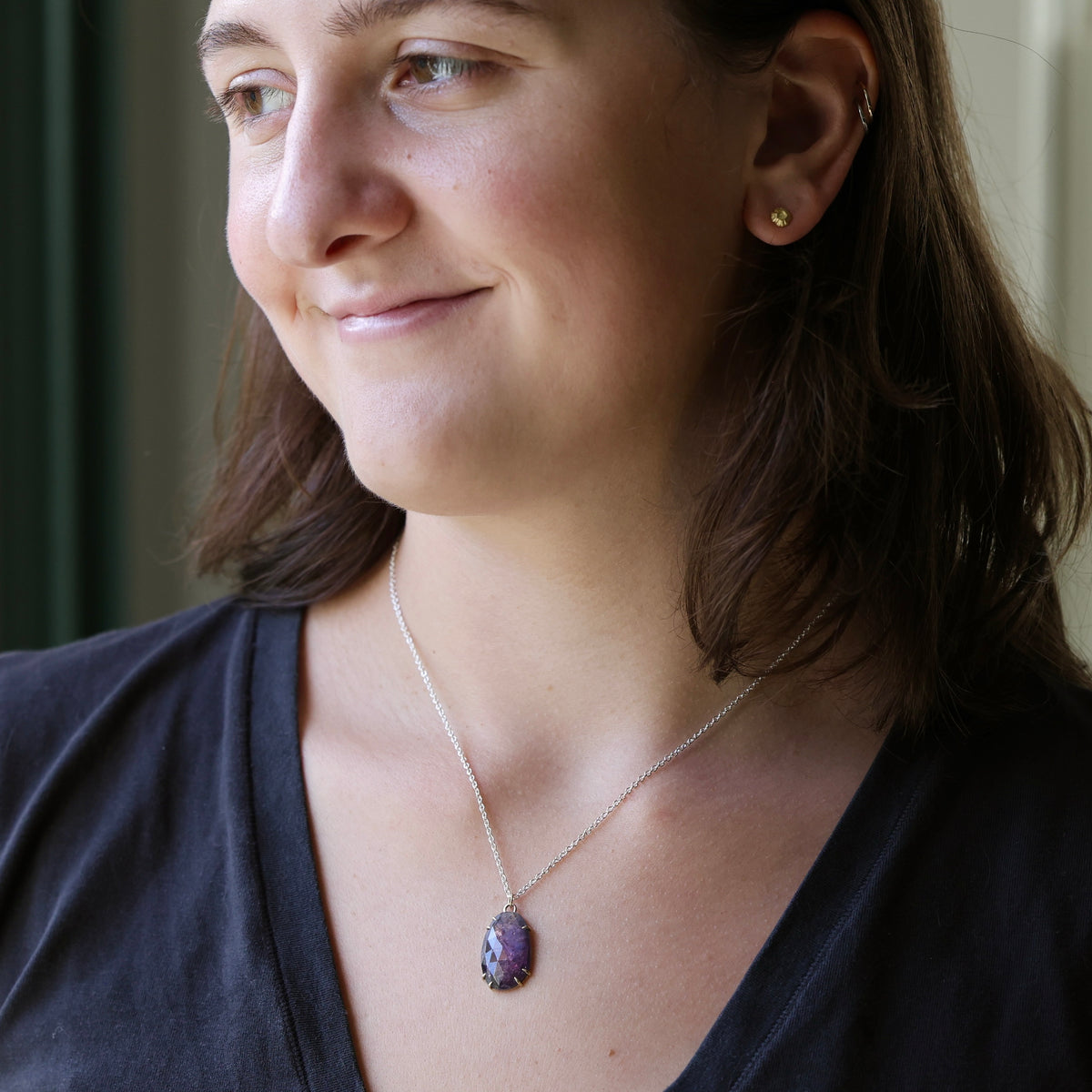 A woman wearing a silver chain necklace with a purple and blue marbled pendant, shown in a close-up profile view.