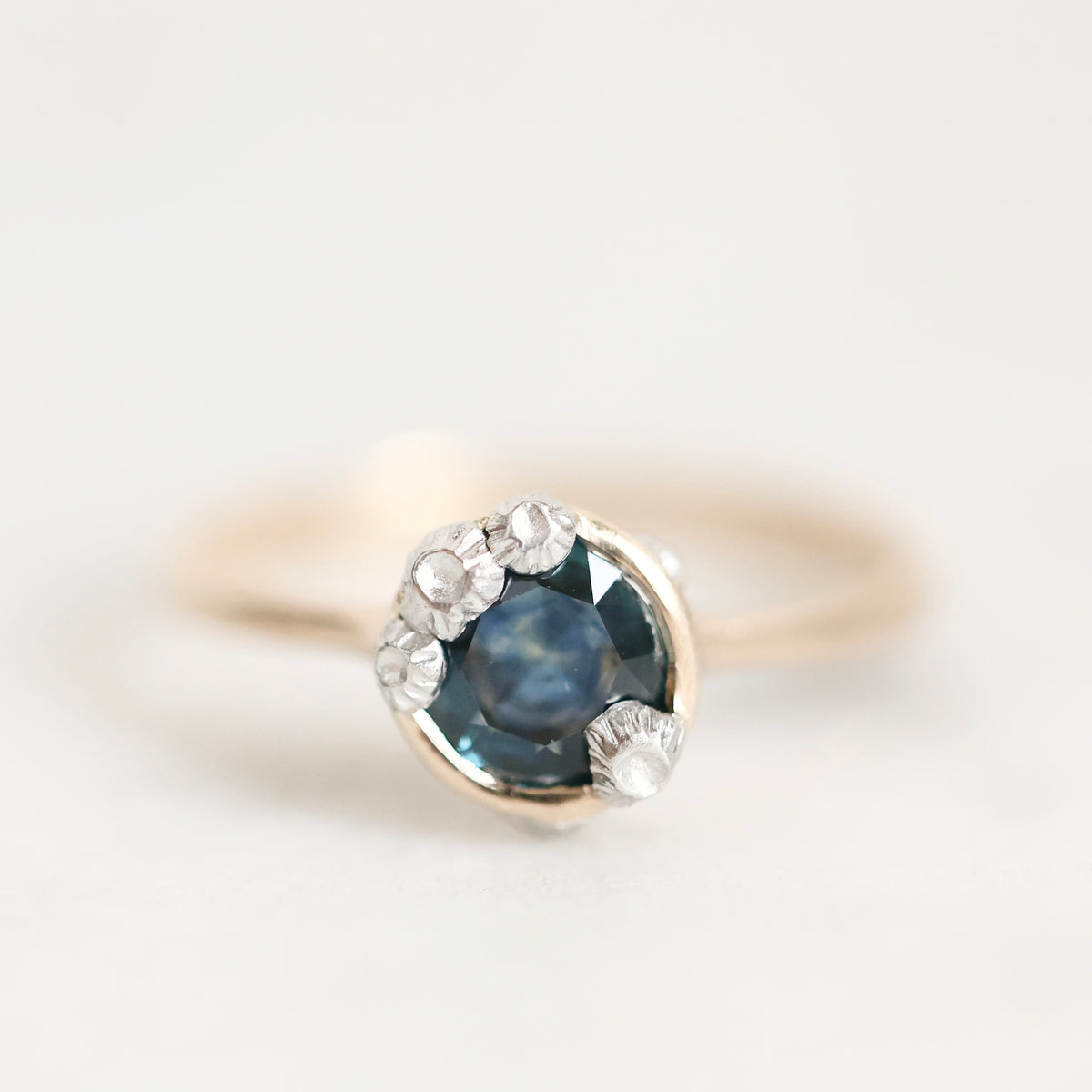 Ring with dark blue stone and lots of barnacles against plain background.
