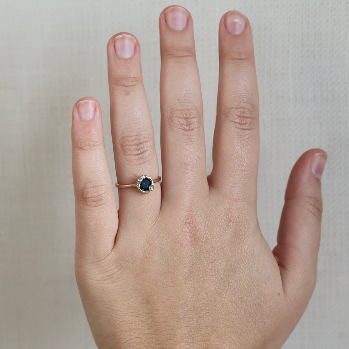 Hand wearing blue stone ring against plain background. 