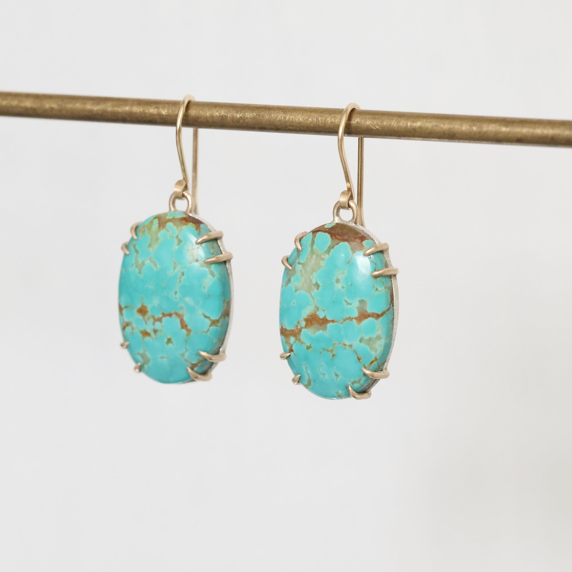 Turquoise earrings on a thin rod against a light gray background