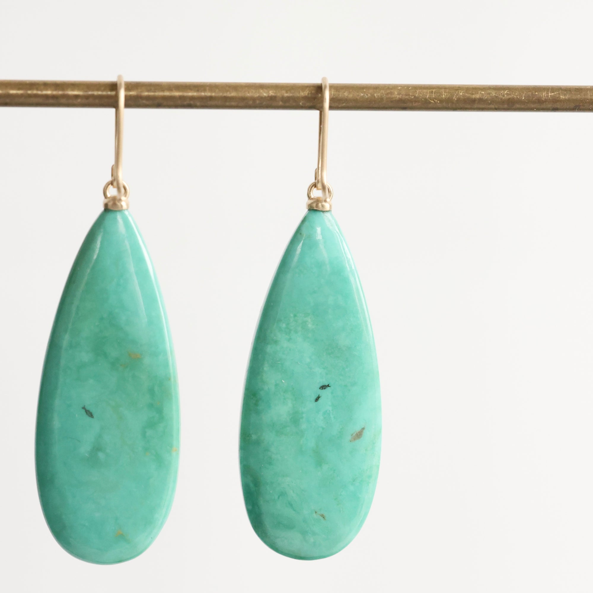 Teardrop-shaped turquoise earrings on a gold earring stand against a white background