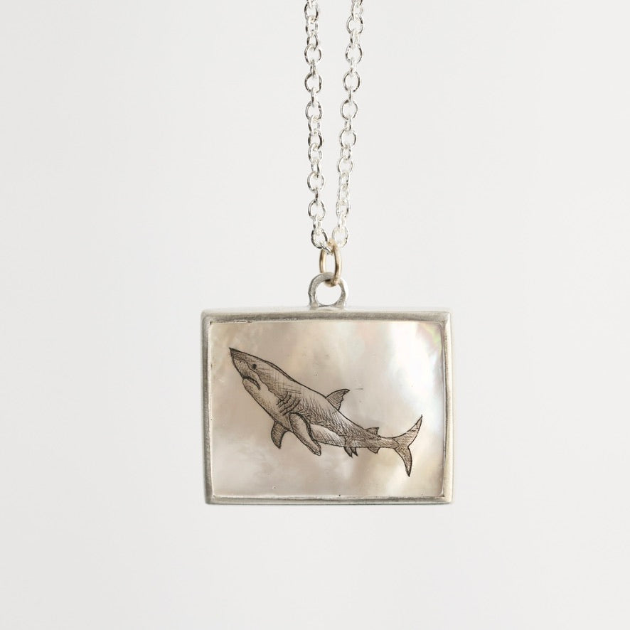 Silver necklace with a square pendant featuring an engraved shark design on a white background