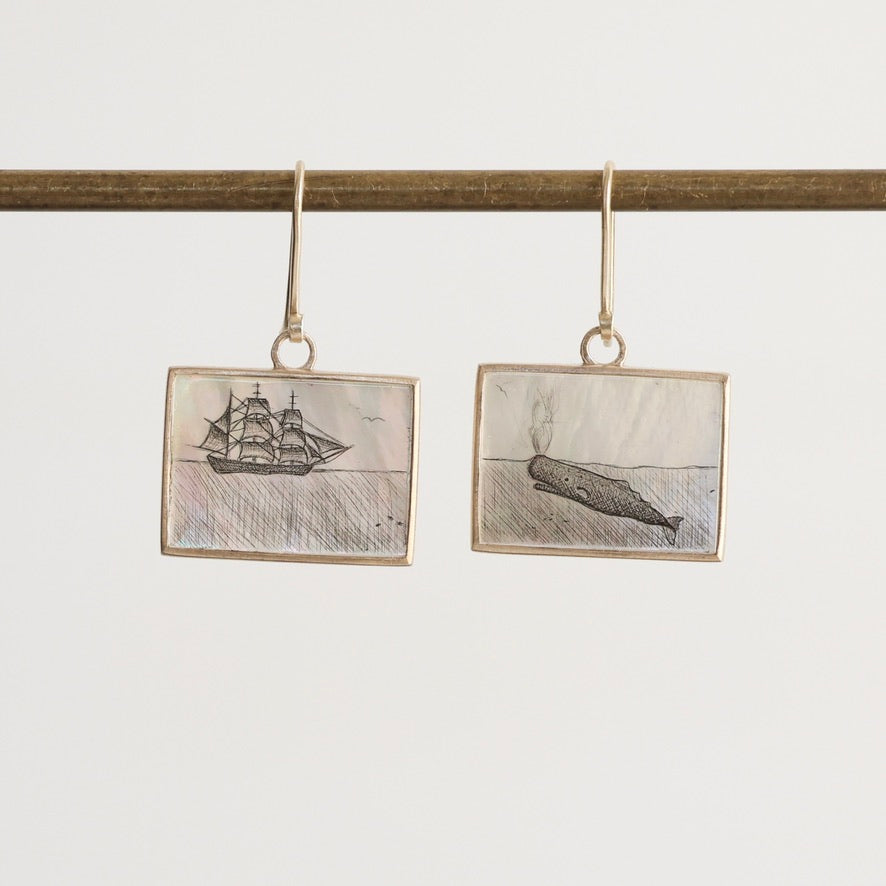 Pair of earrings with ship and whale illustrations on a white background