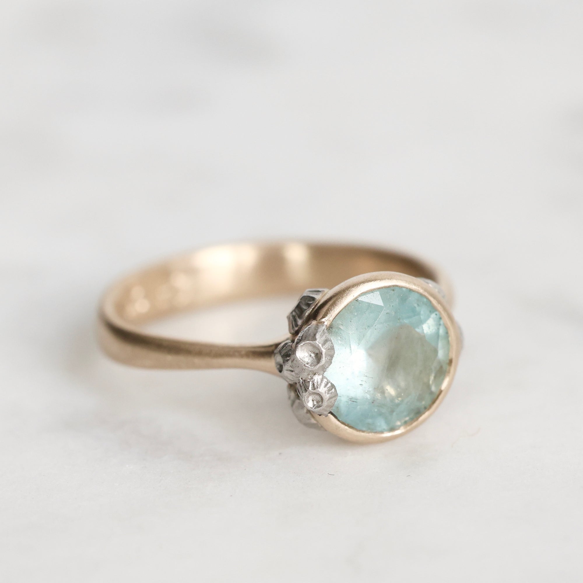 Gold ring with a light blue gemstone on a white background