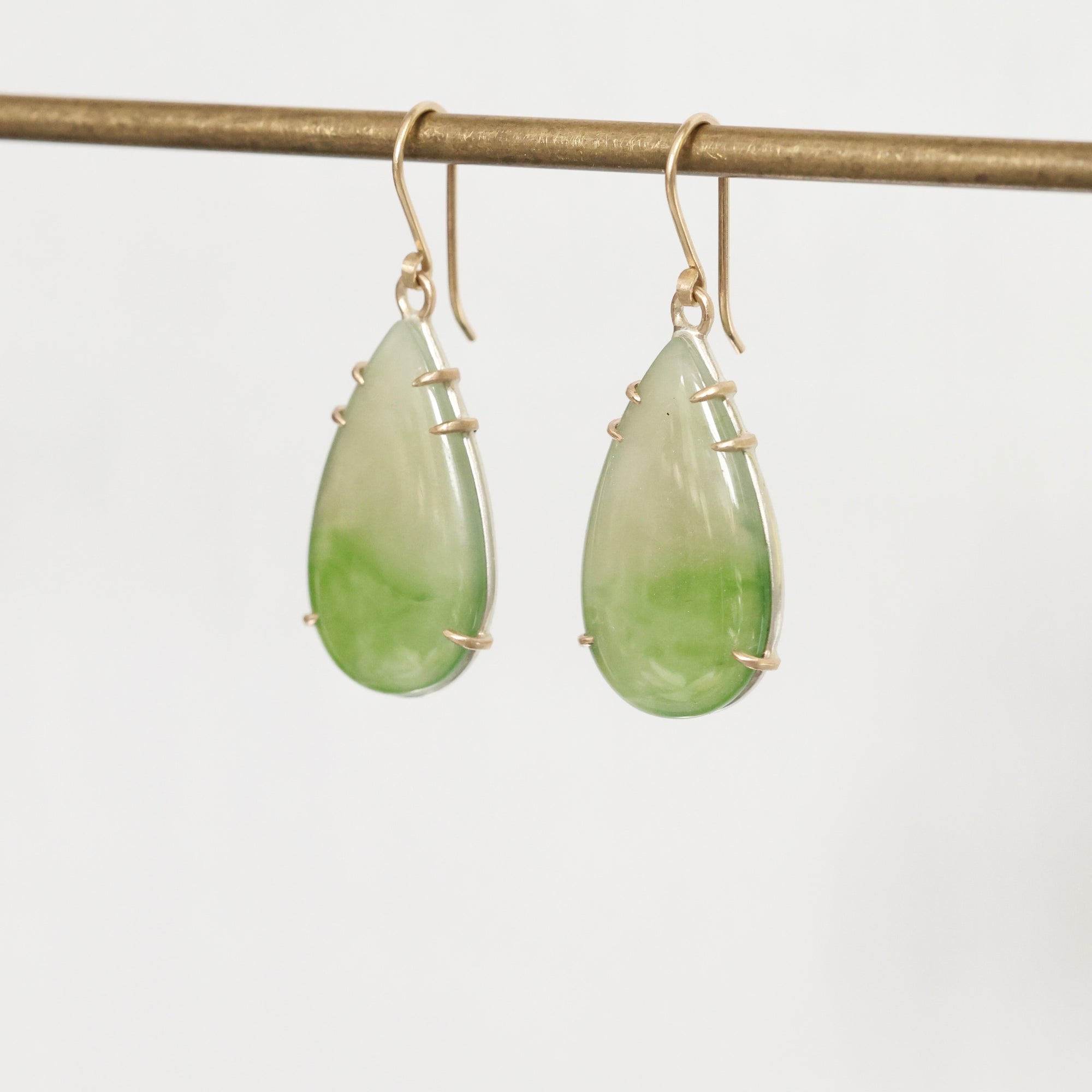 Teardrop-shaped green earrings with gold accents on a white background