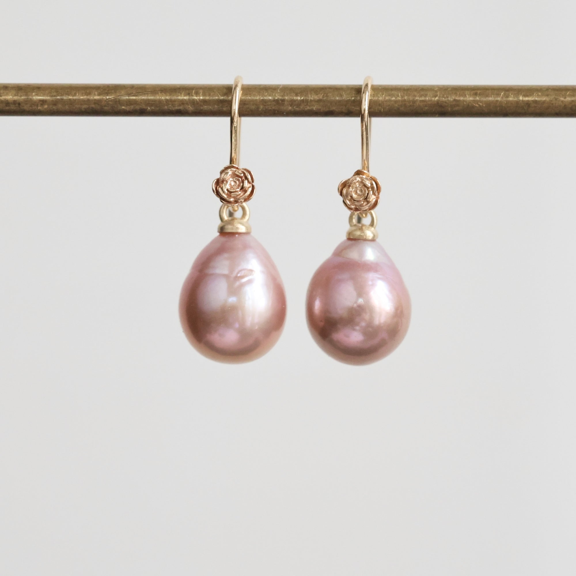 Pair of pink pearl earrings with gold clasps on a light gray background