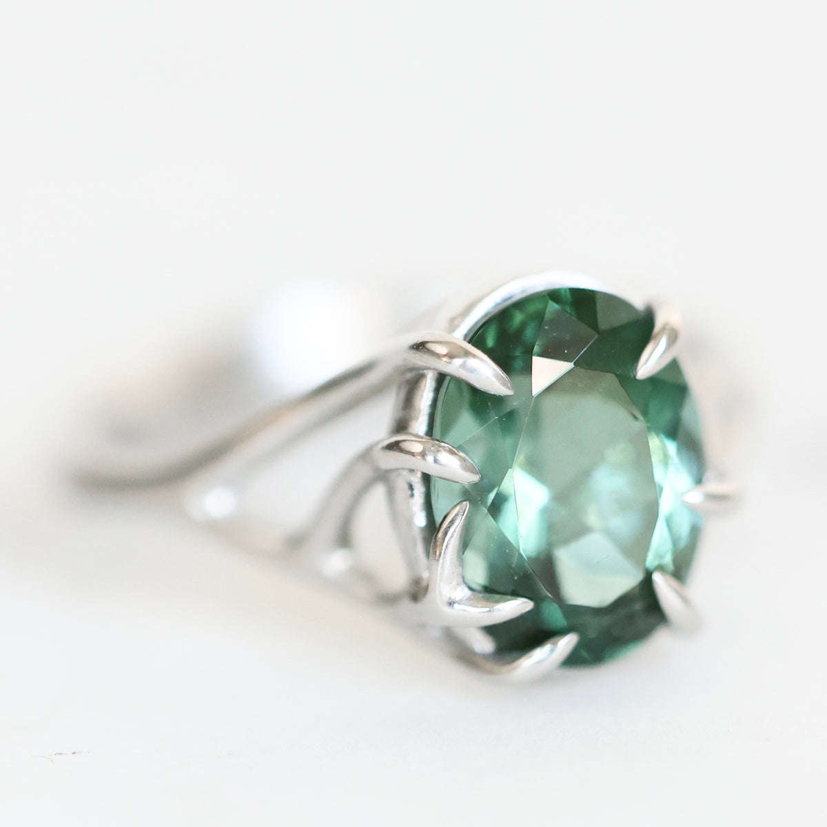 Platinum branchy ring holding green stone.