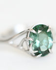 Platinum branchy ring holding green stone.