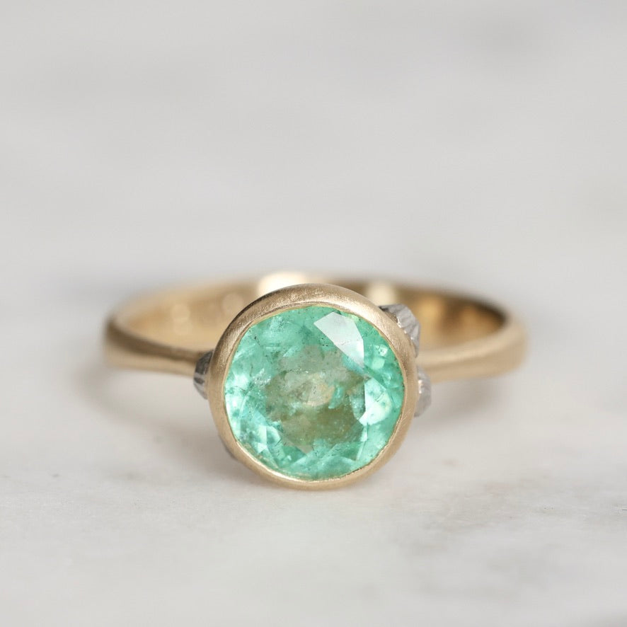 Gold ring with a green gemstone on a light gray background