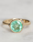 Gold ring with a green gemstone on a light gray background