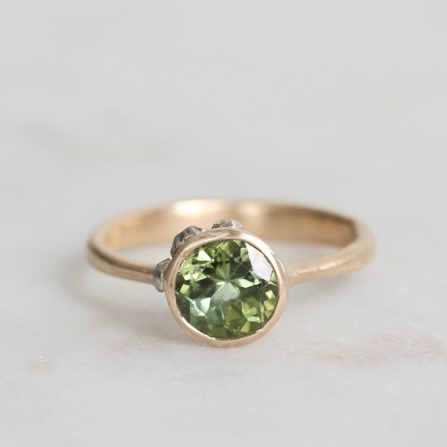 Gold ring with a green gemstone on a light gray background