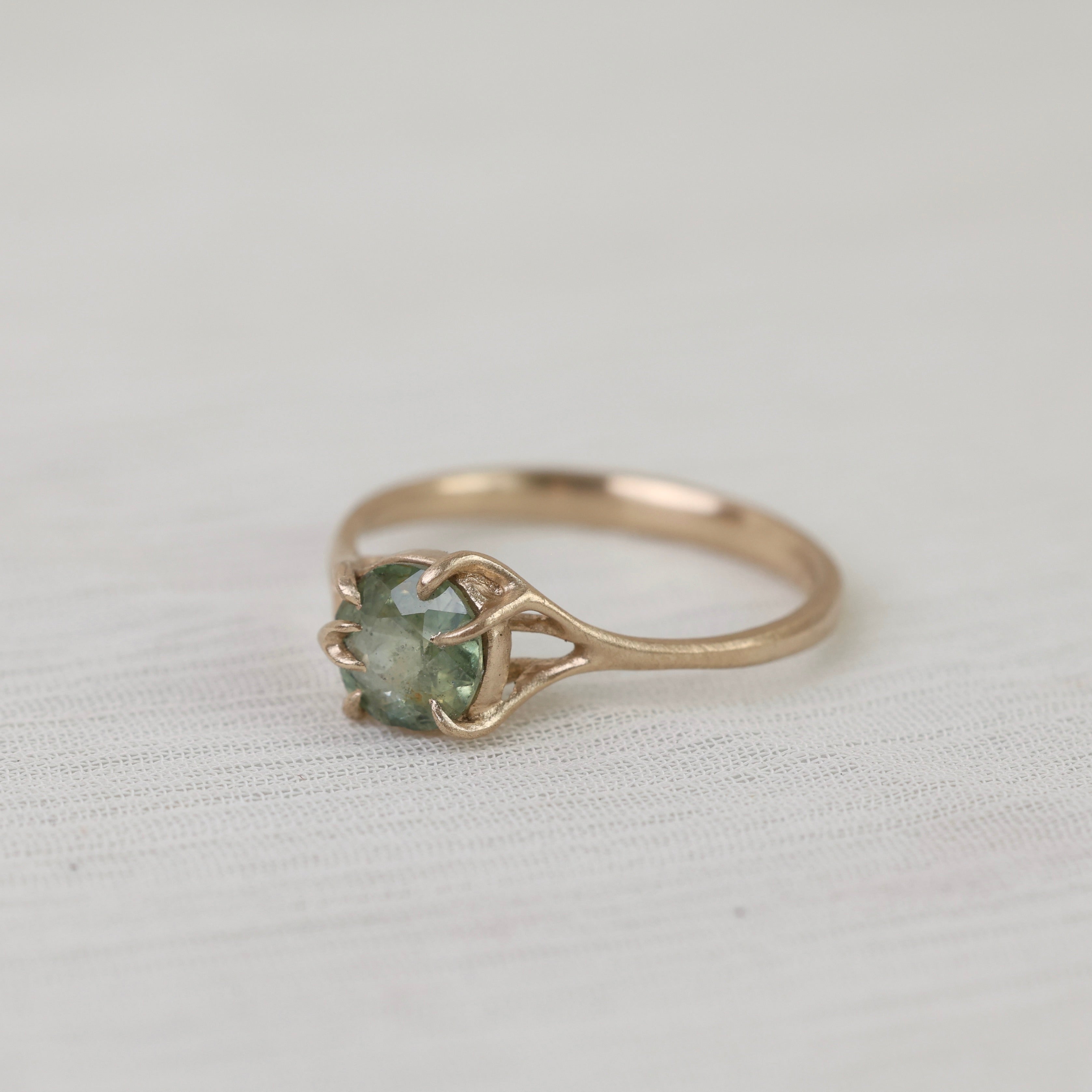 Gold ring with a green gemstone on a light fabric background