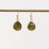 A pair of gold drop earrings with faceted green teardrop-shaped gemstones, hanging from a gold rod against a light gray background.