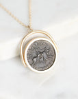 A gold necklace with a circular pendant featuring an antique-style silver coin medallion, displayed on a white marble surface.