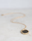 A gold locket necklace with a dark circular medallion, resting on a light marble surface with a soft-focus background.