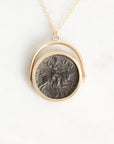 A gold necklace with a circular pendant featuring an antique dark bronze coin, displayed on a clean white background.