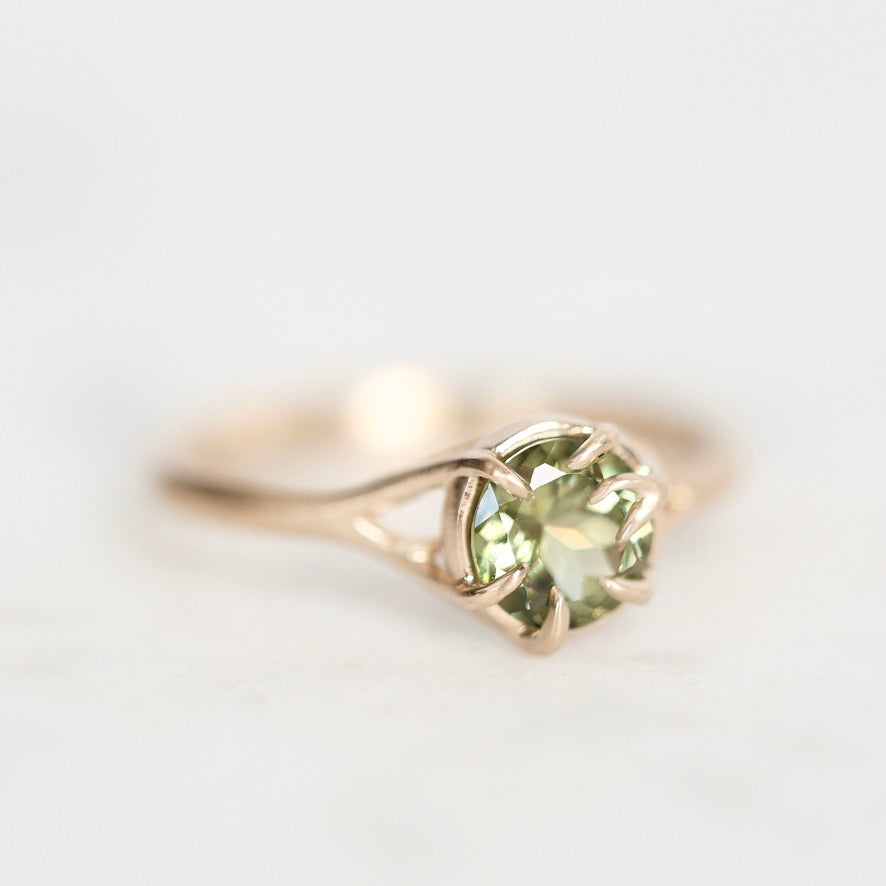 Gold ring with branchy prongs photographed from the side with a bright green gemstone. 
