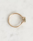 A delicate gold ring with a small green gemstone, photographed from an overhead angle on a light gray marble surface.