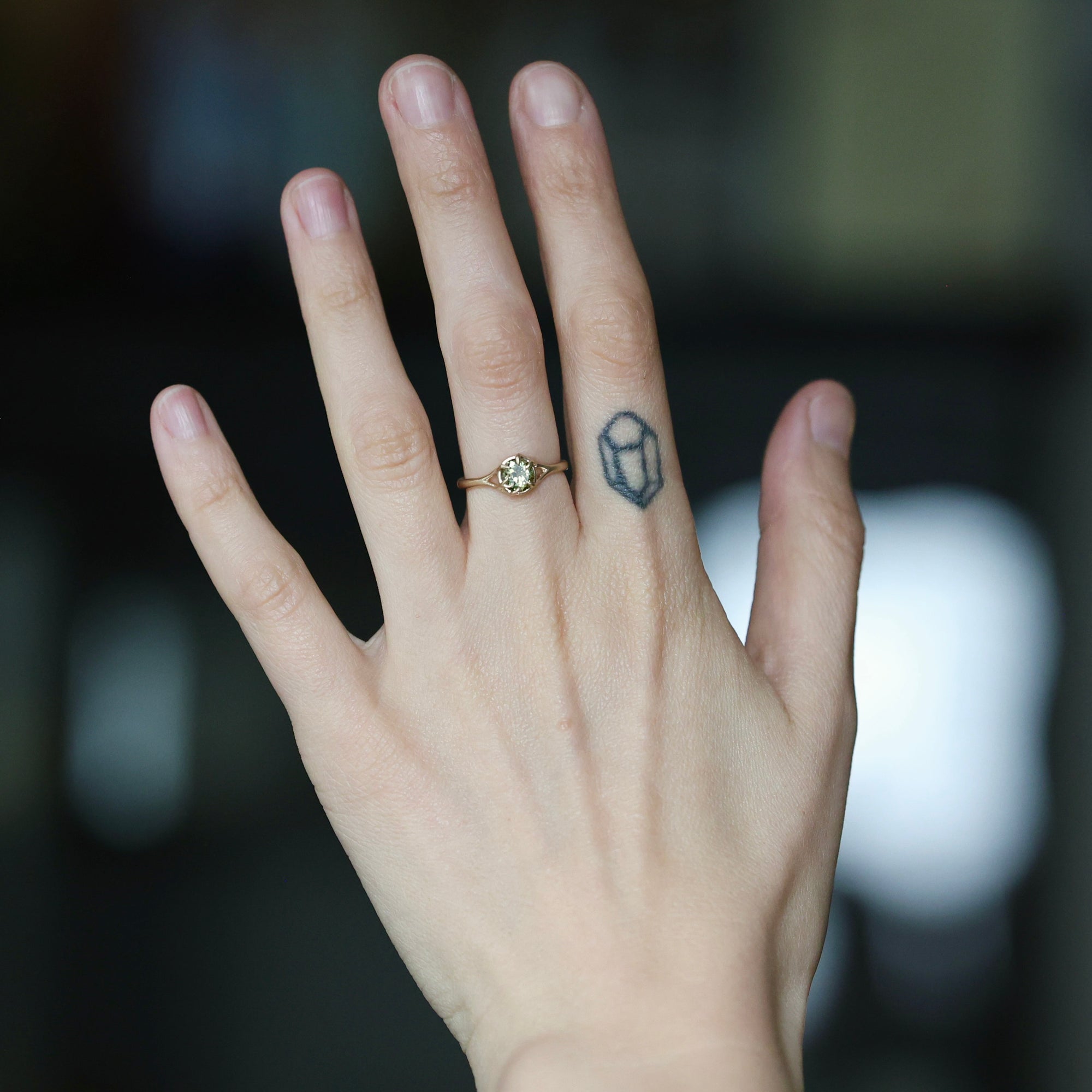 Green gemstone ring on hand with branchy prongs. Hand has large finger tattoo. 