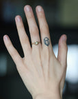 Green gemstone ring on hand with branchy prongs. Hand has large finger tattoo. 