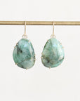 A pair of teardrop-shaped drop earrings with faceted light green and blue marbled gemstones in gold prong settings, hanging from gold hooks on a horizontal gold rod against a plain off-white background.