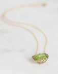 A delicate gold necklace with an oval green gemstone pendant, resting on a light marble surface.