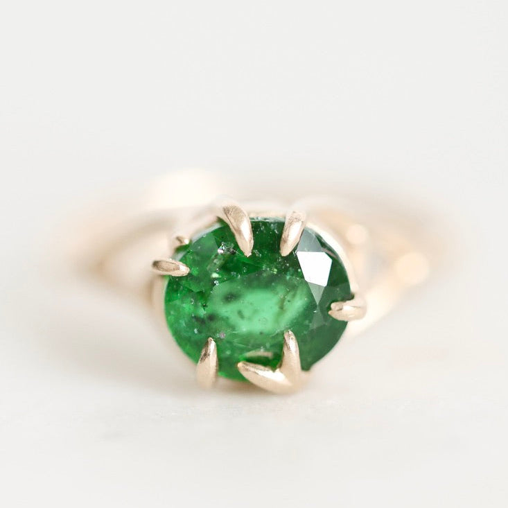 A round-cut green emerald gemstone ring set in a gold prong setting, photographed on a clean white background.