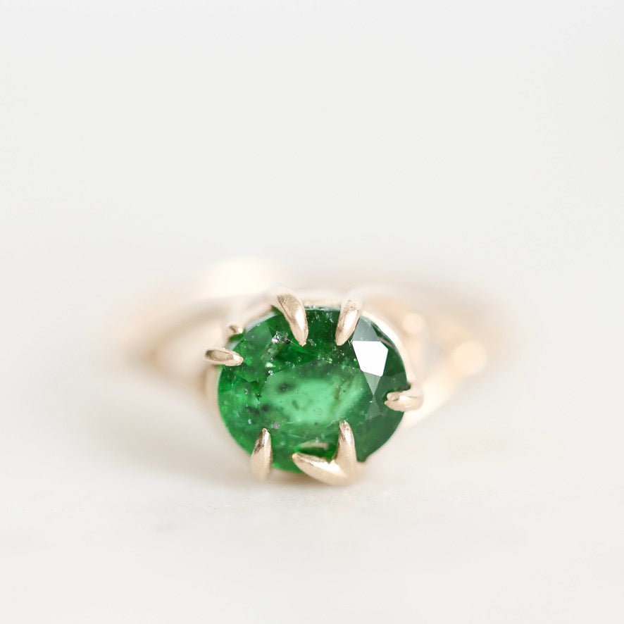 A round-cut green emerald gemstone ring set in a gold prong setting, photographed on a clean white background.